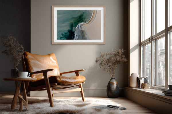 Aerial coastal view of deep teal water curling into pale sand along a sweeping shoreline.