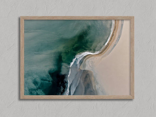 Aerial coastal view of deep teal water curling into pale sand along a sweeping shoreline.