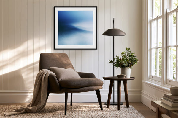 Black-framed blue abstract print above a brown lounge chair, side table, and floor lamp.