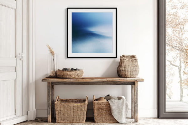 Black-framed blue abstract print above a rustic console table with woven baskets.
