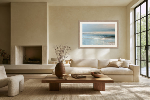 Pale blue coastal abstract in a light wood frame above a cream sofa and low wooden table.