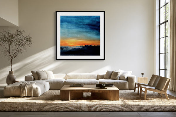 Black-framed abstract sunset print above a cream sectional sofa and low wood coffee table.