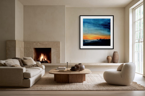 Black-framed abstract sunset print above a low shelf beside a lit stone fireplace.