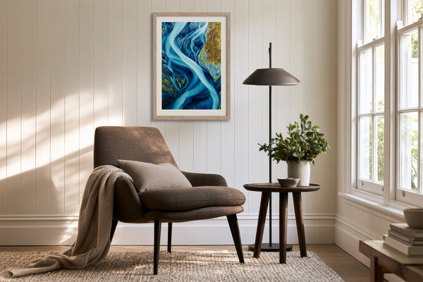 Framed blue glacial river artwork above an armchair, side table, floor lamp, and plant.