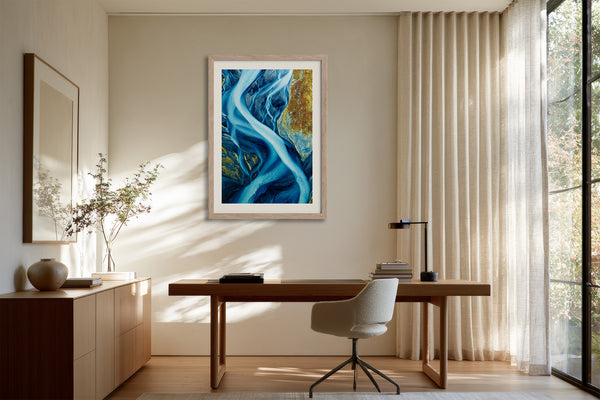 Framed blue glacial river artwork above a wooden desk and upholstered office chair.