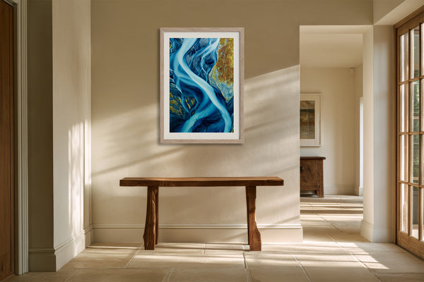Framed blue glacial river artwork above a rustic wooden console table in a sunlit hallway.