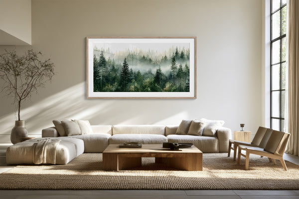 Misty pine forest watercolor in a light wood frame above a cream sectional sofa.