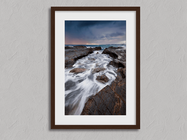 Framed wall art of the Australian coast with rugged rocks, azure sea, and moody skies. A striking coastal landscape print. Ready to hang.