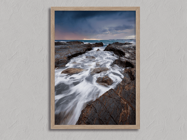 Framed wall art of the Australian coast with rugged rocks, azure sea, and moody skies. A striking coastal landscape print. Ready to hang.