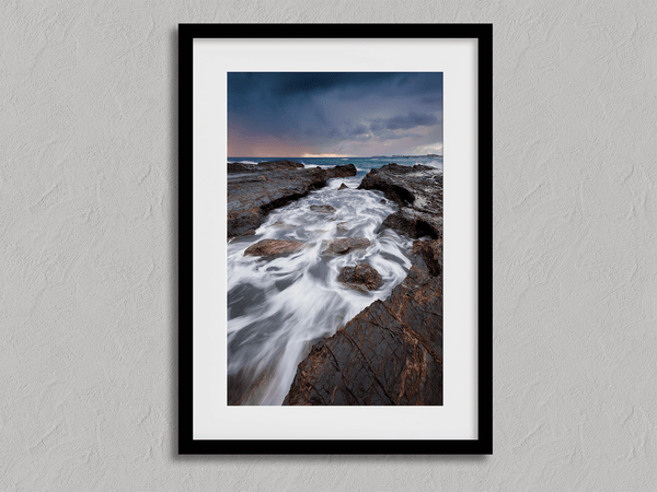Framed wall art of the Australian coast with rugged rocks, azure sea, and moody skies. A striking coastal landscape print. Ready to hang.