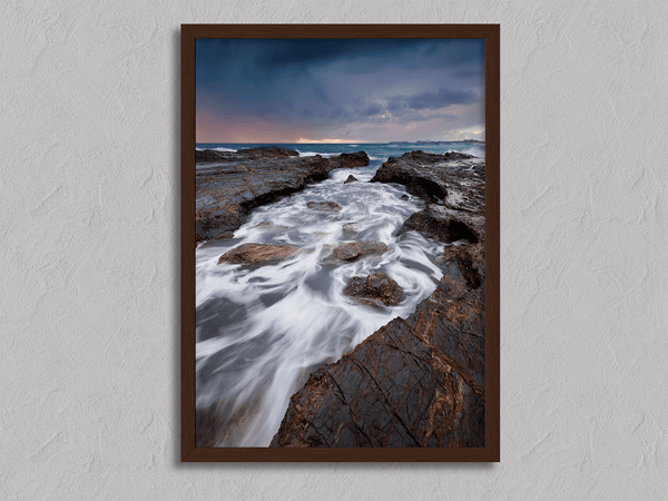 Framed wall art of the Australian coast with rugged rocks, azure sea, and moody skies. A striking coastal landscape print. Ready to hang.