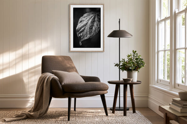 Framed black-and-white wet leaf artwork above an upholstered armchair and side table.