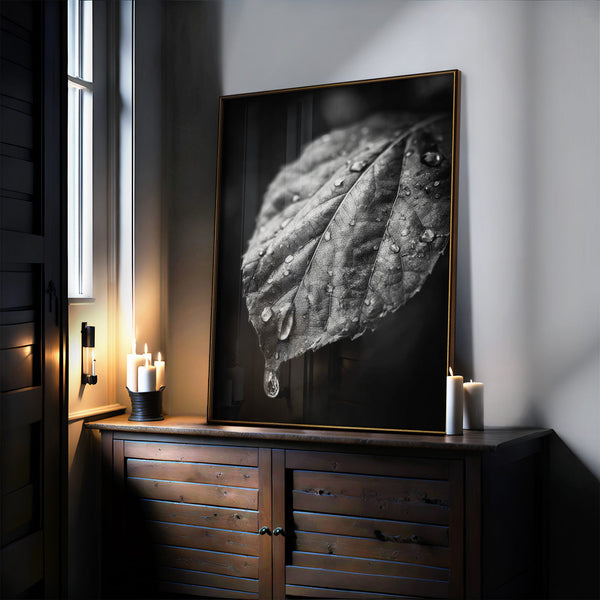 Large black-framed raindrop-covered leaf artwork leaning on a dark wooden cabinet with candles.