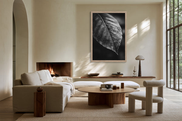 Framed black-and-white leaf vein photograph above a fireplace and curved wood coffee table.