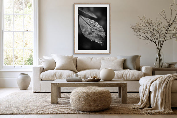 Light-framed black-and-white leaf wall art above a cream sofa, coffee table, and woven ottoman.
