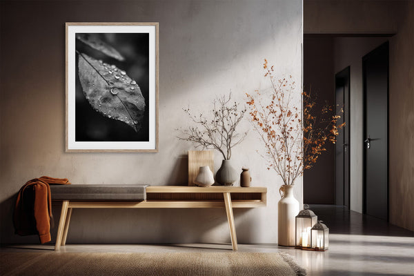 Light-framed dew-covered leaf wall art above a wooden console with vases and dried branches.