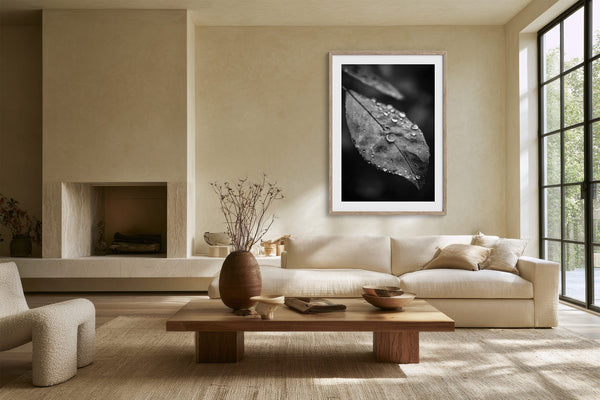 Light wood-framed dew-covered leaf wall art above a cream sofa and low wooden coffee table.