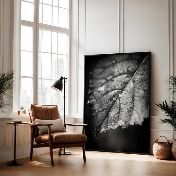 Large unframed black-and-white leaf print leaning beside a leather armchair and floor lamp.