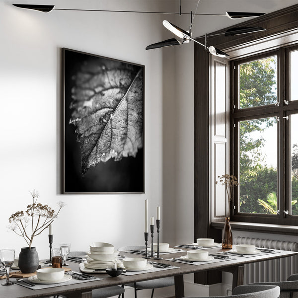 Black-framed monochrome leaf artwork displayed above a set dining table near a large window.