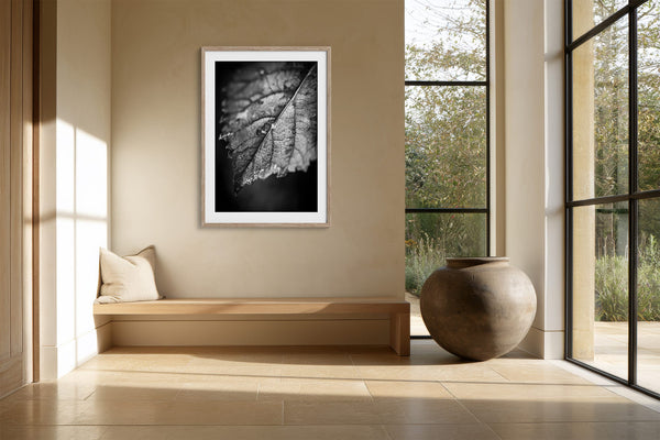 White-matted leaf print in a light wood frame above a built-in bench.