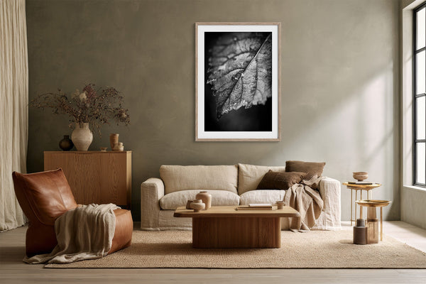 White-matted black-and-white leaf print centered above a cream sofa and wood coffee table.