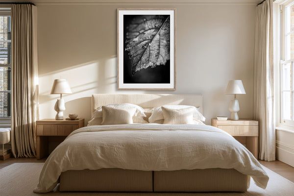 White-matted monochrome leaf artwork above a bed between matching bedside lamps.