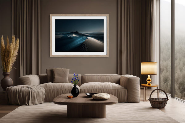 Matted desert dune artwork in a light wood frame above a beige sofa and round coffee table.