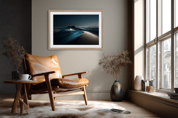 Matted desert dune print in a light wood frame above a leather lounge chair.