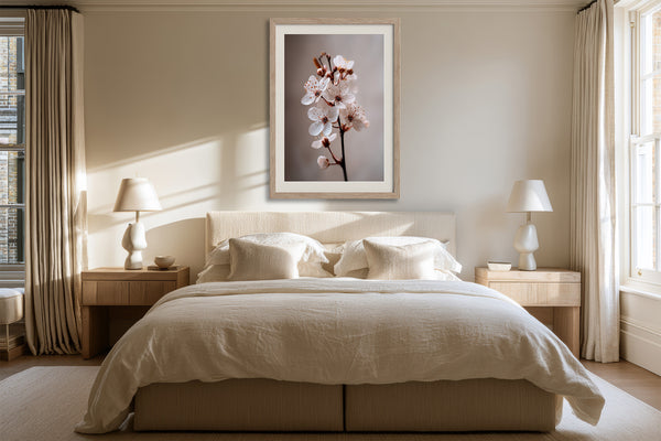 Light wood-framed cherry blossom print centered above a bed with cream bedding.