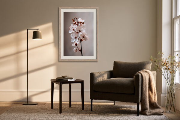 Light wood-framed cherry blossom print above a dark armchair, side table, and floor lamp.