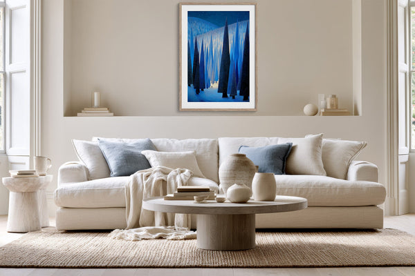 White-framed blue forest print above a white sofa and round wooden coffee table.
