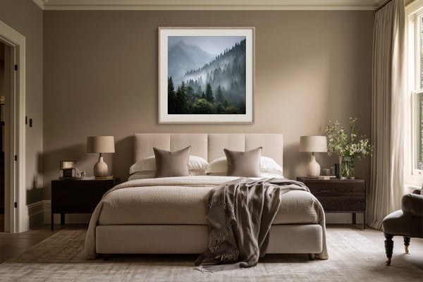 Framed misty mountain forest artwork centered above a beige bed with dark wood nightstands.