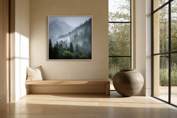 Framed misty mountain forest artwork above a built-in bench beside tall black-framed windows and a large urn.