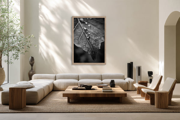 Framed black-and-white raindrop-covered leaf photograph above a cream sectional sofa and low wooden table.