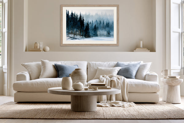 Framed winter forest artwork above a white sofa with blue-gray cushions.