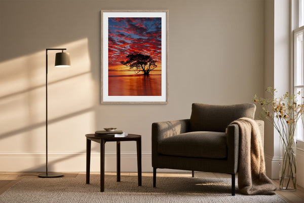 Light wood-framed sunset tree print above an armchair, side table, and floor lamp.