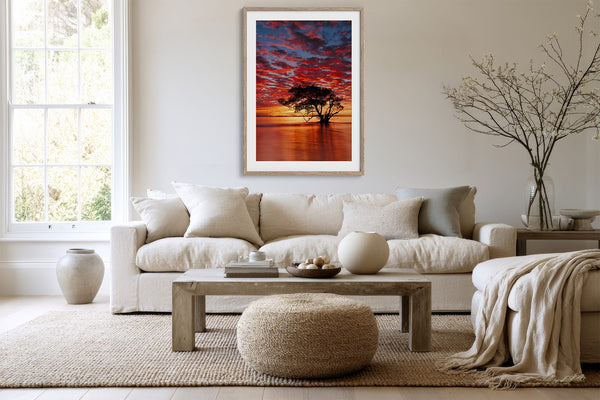 Light wood-framed sunset tree print above a white sofa, coffee table, and textured ottoman.