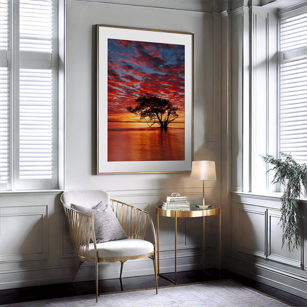 Thin gold-framed sunset tree print above a gold chair and glass side table.