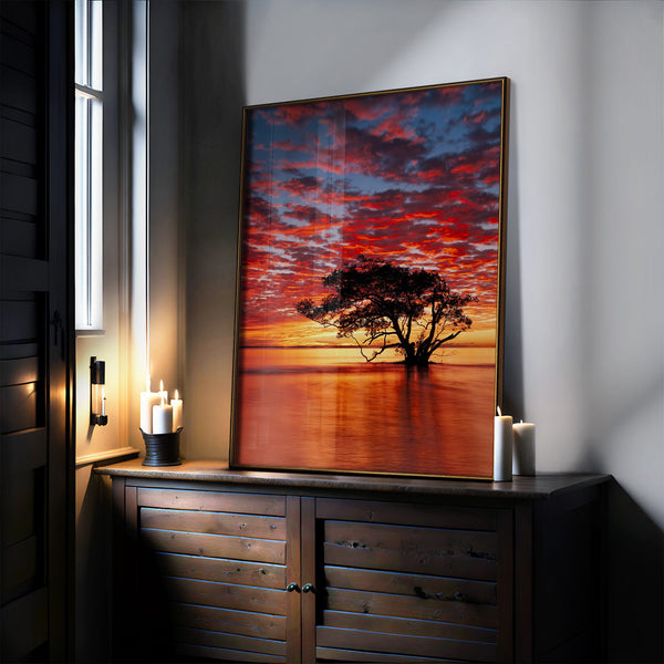 Large thin-framed sunset tree artwork leaning on a dark cabinet beside lit candles.