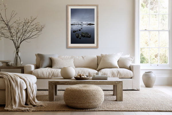Light wood-framed mountain lake artwork above a cream sofa and wooden coffee table.
