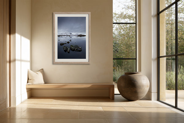 Light wood-framed mountain lake artwork above a built-in bench beside large grid windows.