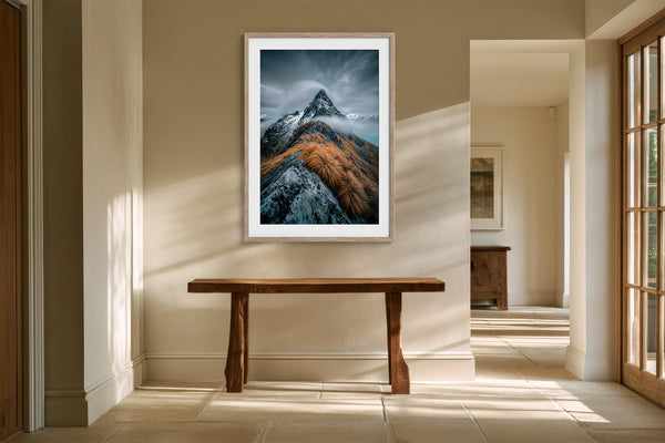 Framed mountain print above a wooden console table in a sunlit hallway.