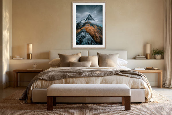 Framed mountain print centered above a bed with neutral bedding and bedside tables.