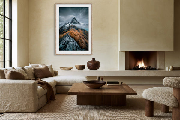 Framed mountain print above a sofa and coffee table beside a lit fireplace.