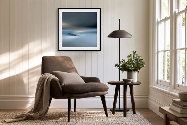 Black-framed Low Tide Light coastal print above a brown lounge chair, side table, and floor lamp.