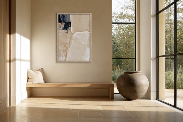 Framed beige and charcoal abstract artwork above a built-in bench beside large windows.