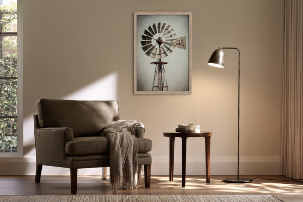 Framed windmill artwork above an upholstered armchair, side table, and black floor lamp.