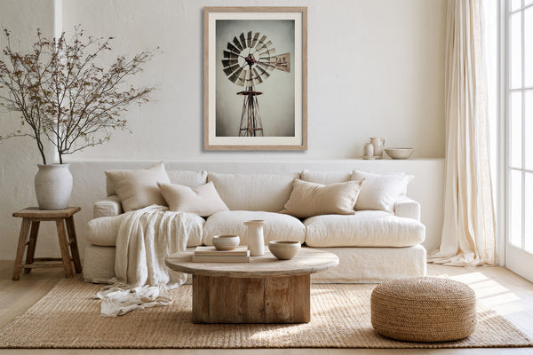 Light wood-framed windmill artwork above a white sofa with a rustic round coffee table.