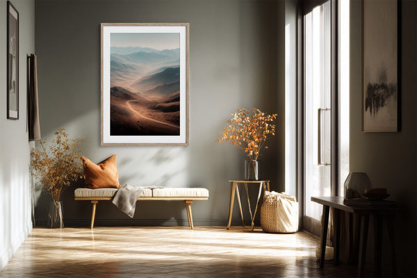 Light wood-framed mountain valley artwork above a cushioned bench beside tall windows.