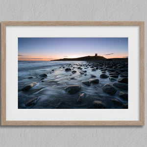 Ethereal Dawn coastal wall art featuring Northumbrian castle ruins, rocky shoreline and calm sea at sunrise